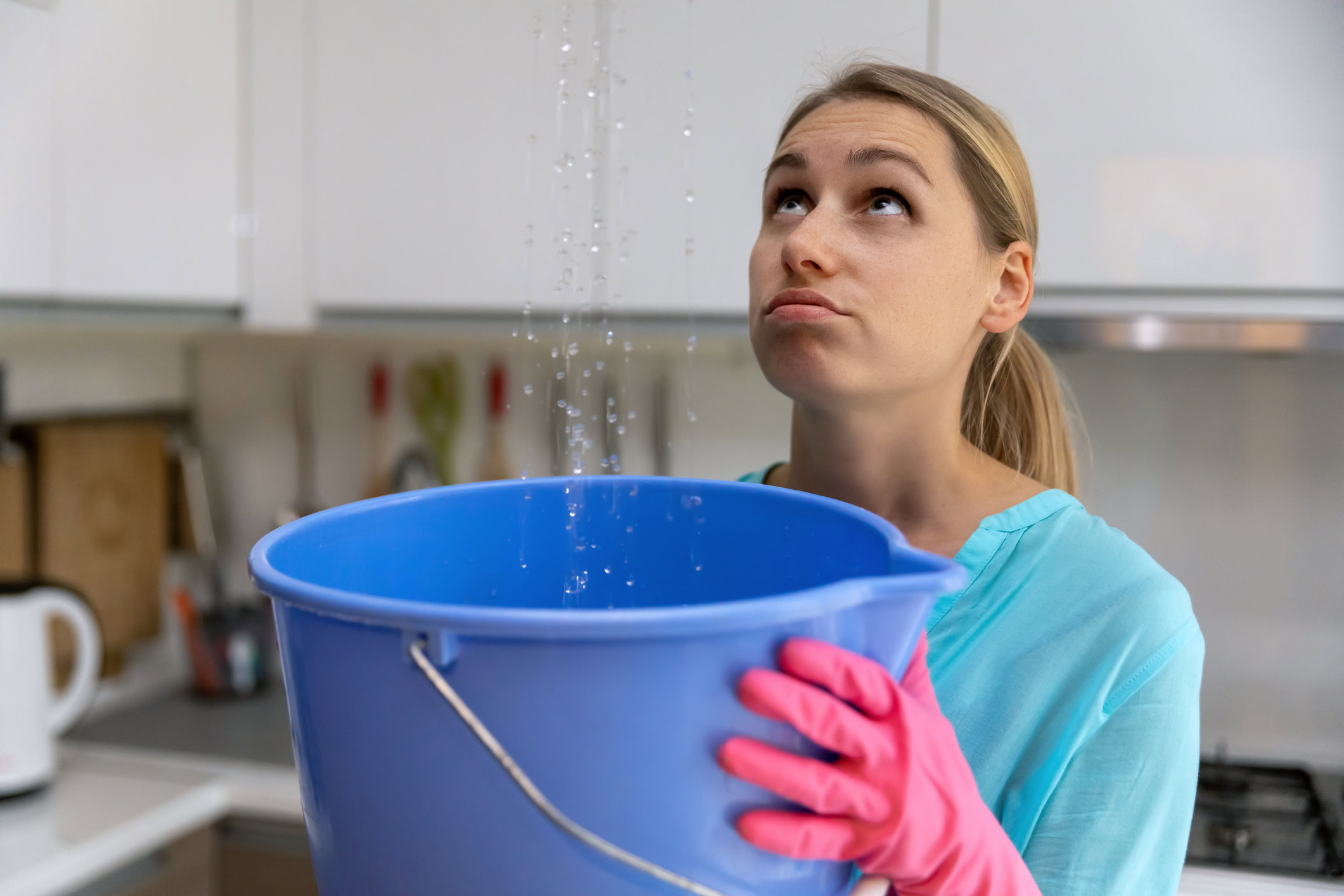 Woman holding bucket while water leaks from ceiling into kitchen