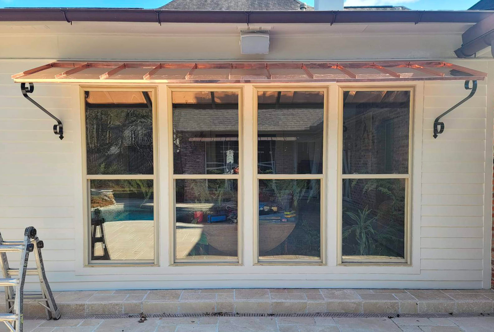 Four large windows with light trim beneath a new copper metal awning