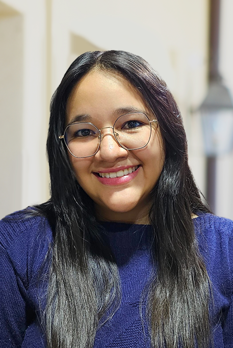 A woman with long dark hair and glasses smiles at the camera in a navy sweater—join our team and share this welcoming energy.