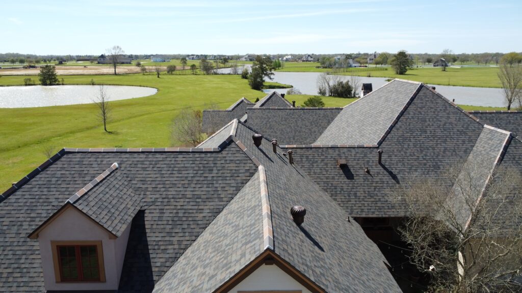 Aerial view of a house with an Owens Corning roof deployment, gray shingles, lush lawns, trees, and ponds in the background.